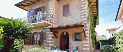 A two-story building with a balcony, outdoor seating area, and potted plants.