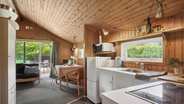A compact kitchen with wooden walls, a dining area with a table and chairs, a refrigerator, a microwave, and a window providing a view of greenery. - Awesome home in Eskebjerg with WiFi (Eskebjerg)
