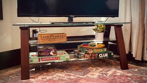 A glass-top table with board games, a television, and a sign for Land O'Lakes. - Charming 1BR riverside cabin in Brainerd, MN. River sunsets, stocked kitchenette, fire pit, 10 min to downtown. Ideal for couples, small families & remote workers seeking a peaceful Up North escape. (Daggett Brook Township)