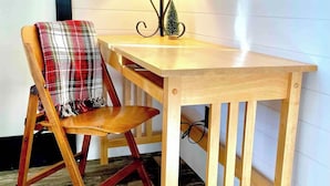 A wooden table with a lamp, a plaid chair, and a small Christmas tree on the table. - Charming 1BR riverside cabin in Brainerd, MN. River sunsets, stocked kitchenette, fire pit, 10 min to downtown. Ideal for couples, small families & remote workers seeking a peaceful Up North escape. (Daggett Brook Township)