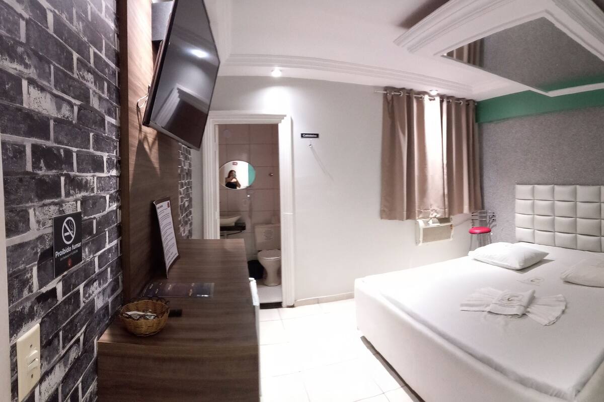 Habitación de hotel con una cama grande, un televisor montado en la pared, un baño pequeño y una pared de acento verde.