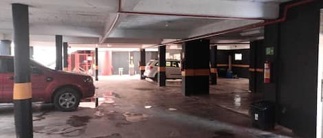 A parking garage with wet floors, concrete pillars, and a few parked cars.