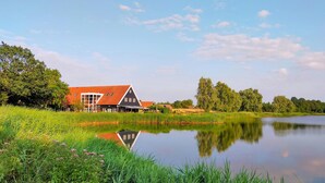 Ein traditionelles niederländisches Haus mit rotem Dach, gelegen an einem ruhigen See, umgeben von üppigem Grün.