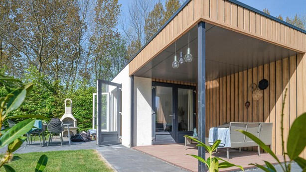 Ein modernes Haus mit überdachter Terrasse, Grill und Sitzbereich mit Bank und Tisch.