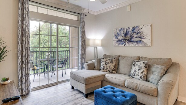 A living room with a sectional sofa, a blue ottoman, a floor lamp, and a large window with curtains. - 10 Mi to Disney! Family-Friendly Resort Getaway (Davenport)