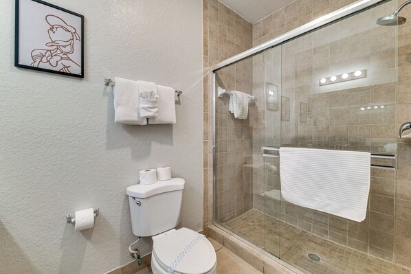 Un baño con inodoro, ducha con puerta de vidrio y un cuadro en la pared.