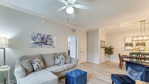 A modern living room with a grey sofa, blue ottoman, and a dining area with a wooden table and chairs. - 10 Mi to Disney! Family-Friendly Resort Getaway (Davenport)