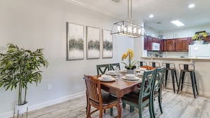 A dining area with a wooden table set for six, surrounded by green chairs. There is a potted plant to the left and a chandelier above. - 10 Mi to Disney! Family-Friendly Resort Getaway (Davenport)