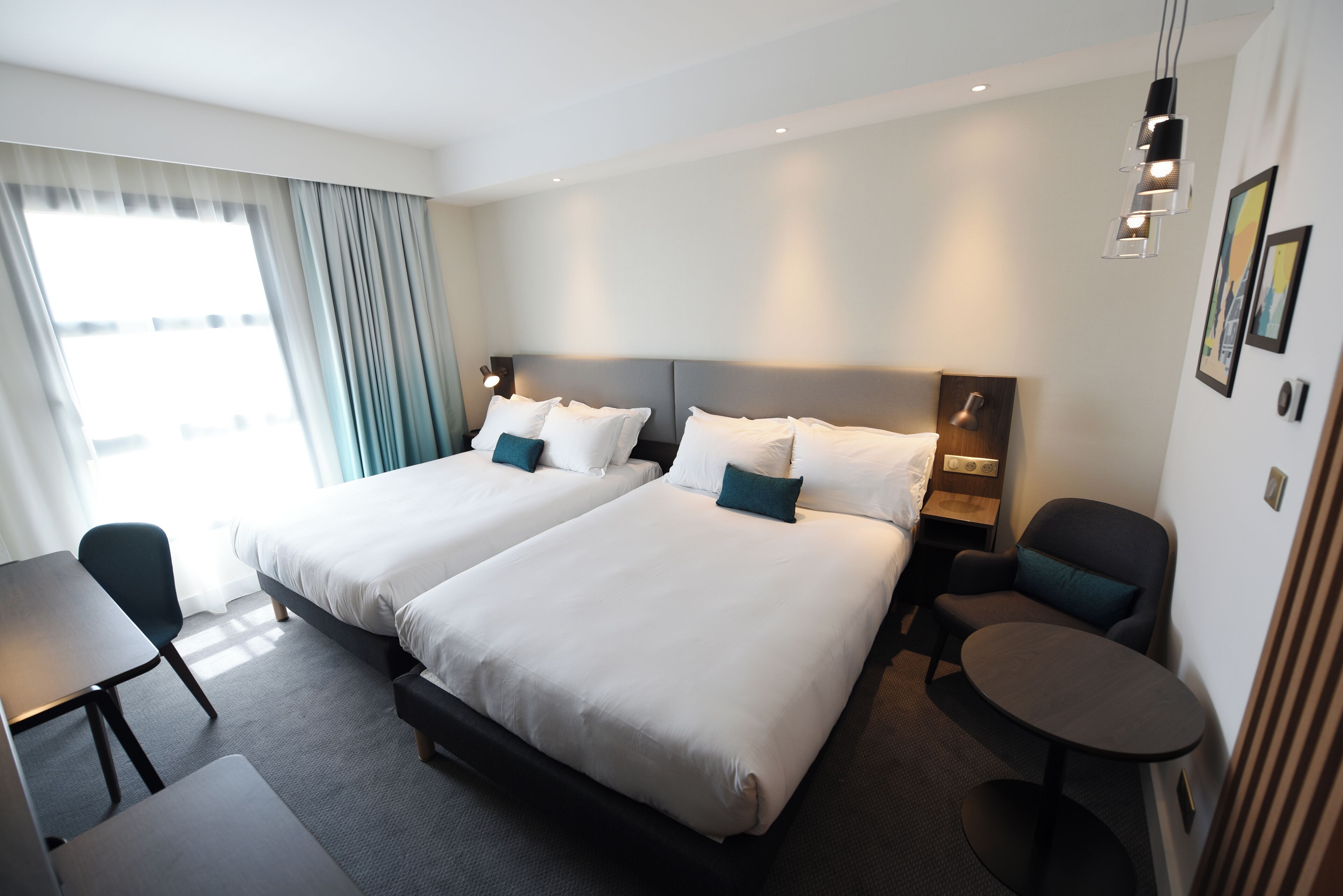 A hotel room with two beds, a desk, a chair, and a small table.