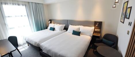 A hotel room with two beds, a desk, a chair, and a small table.