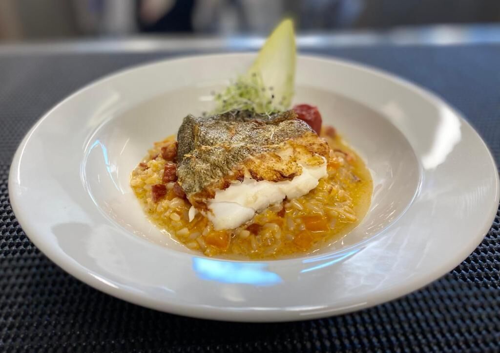 Un plato de comida con pescado, patatas y una guarnición sobre un plato blanco.