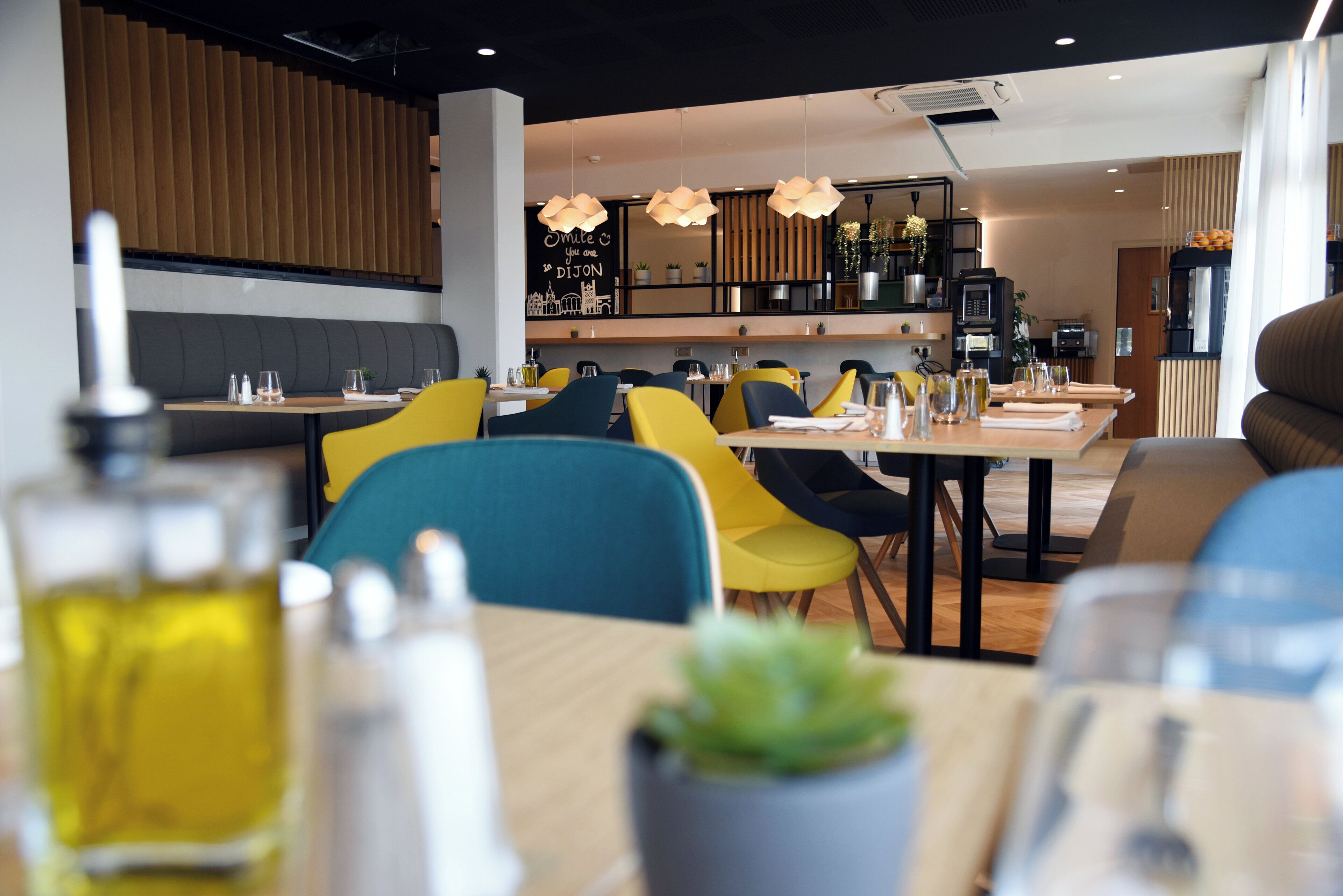 Un restaurante moderno con sillas amarillas y azules, paneles de madera e iluminación colgante.