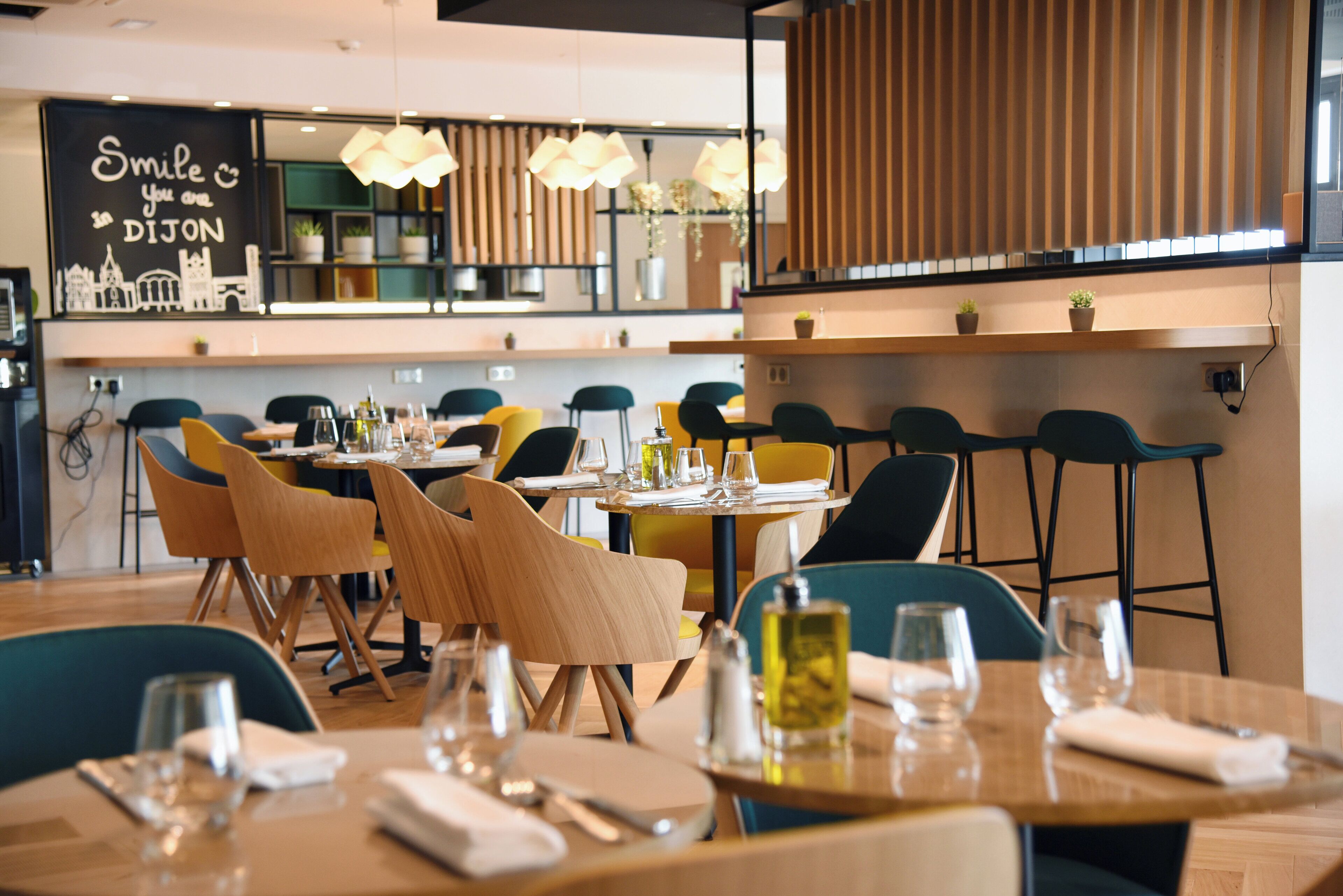 Ein Restaurantinneres mit mehreren Tischen und Stühlen, einer Tafel mit einer Beschriftung und hängenden Pendelleuchten.