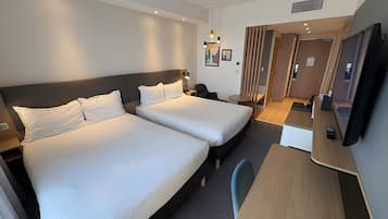 A hotel room with two beds, a desk, a chair, a TV, and a small table.