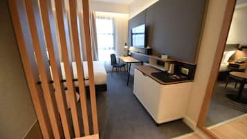 A compact hotel room with a kitchenette, a desk, a chair, and a bed.