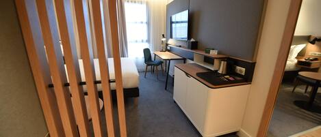 A compact hotel room with a kitchenette, a desk, a chair, and a bed.