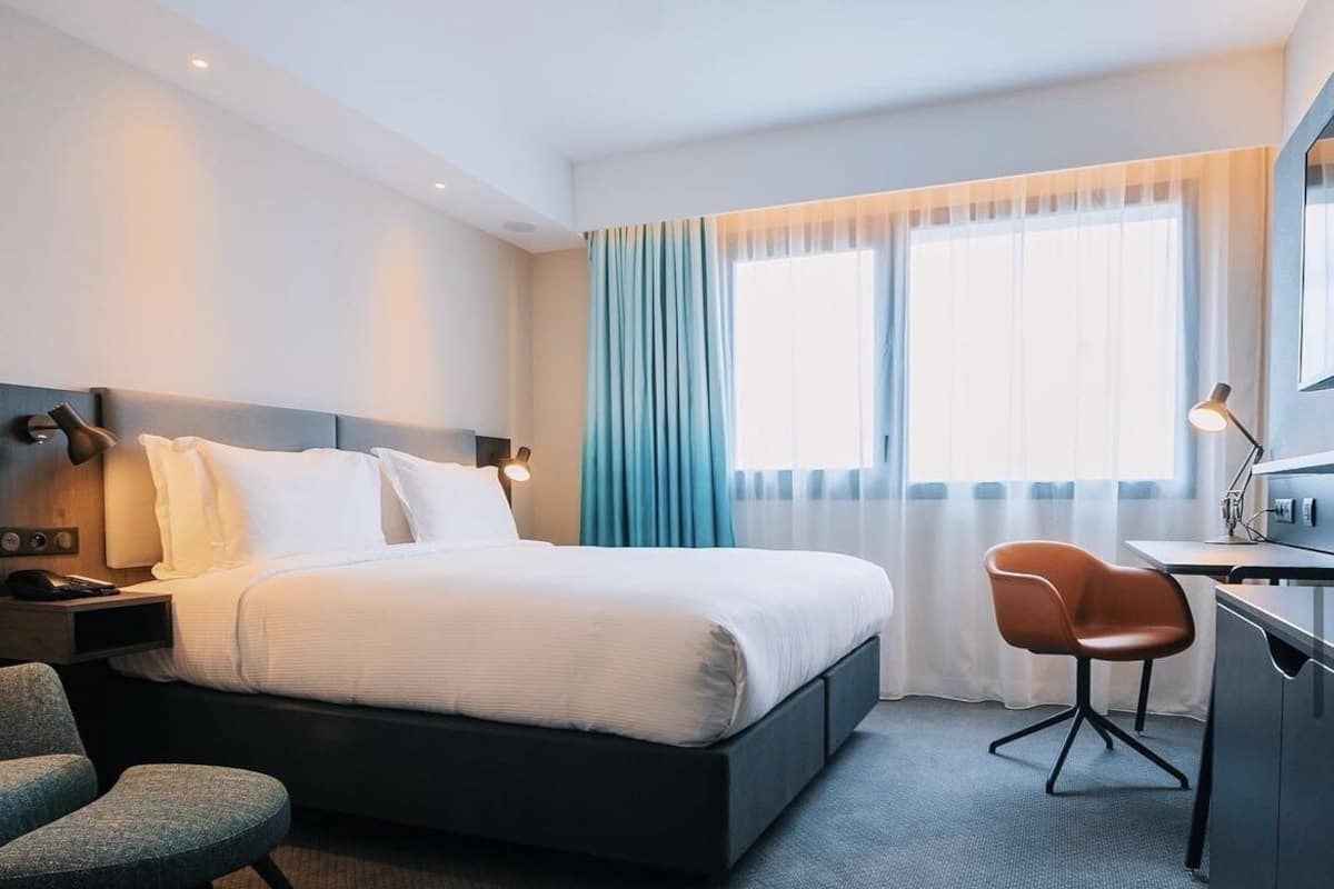 A modern hotel room with a large bed, a desk, and a chair.