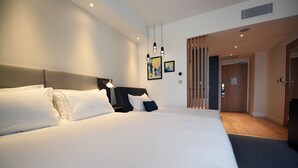 A modern hotel room with a large bed, a bedside table, and a wall-mounted light fixture. - Holiday Inn Dijon Sud Longvic by IHG (Longvic)