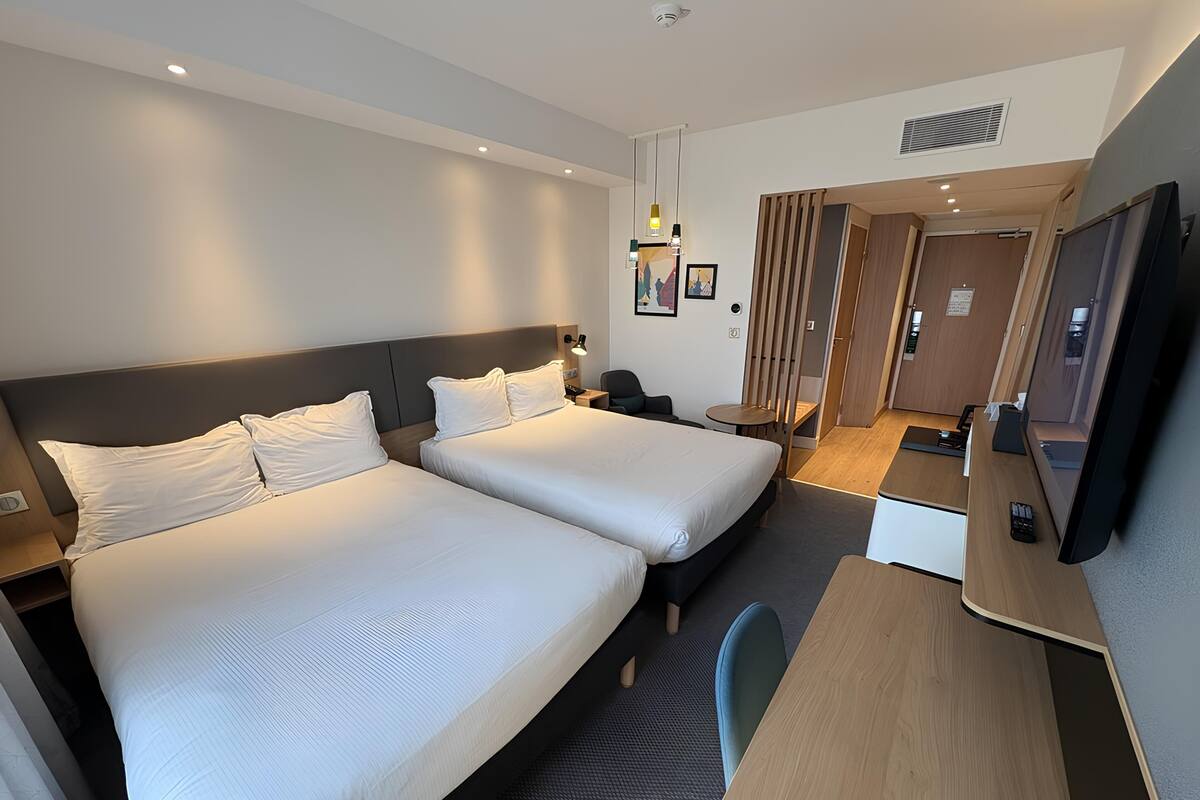 A hotel room with two beds, a desk, a chair, a TV, and a small table.