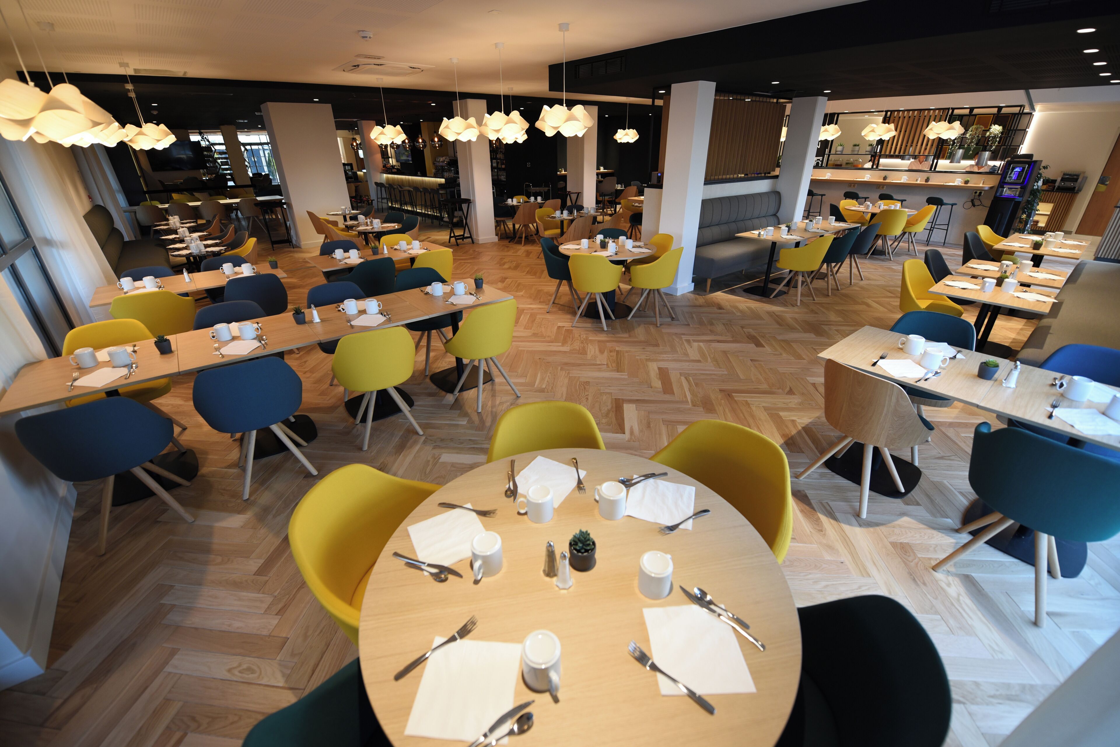 Een modern restaurant met ronde tafels en kleurrijke stoelen, houten vloeren en hanglampen.