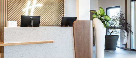 Un mostrador de recepción de diseño moderno, con una pared de estampado geométrico, dos monitores y una planta en maceta.