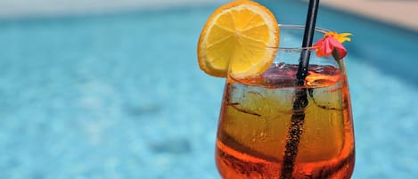 A cocktail with a slice of orange and a flower garnish, placed near a pool.