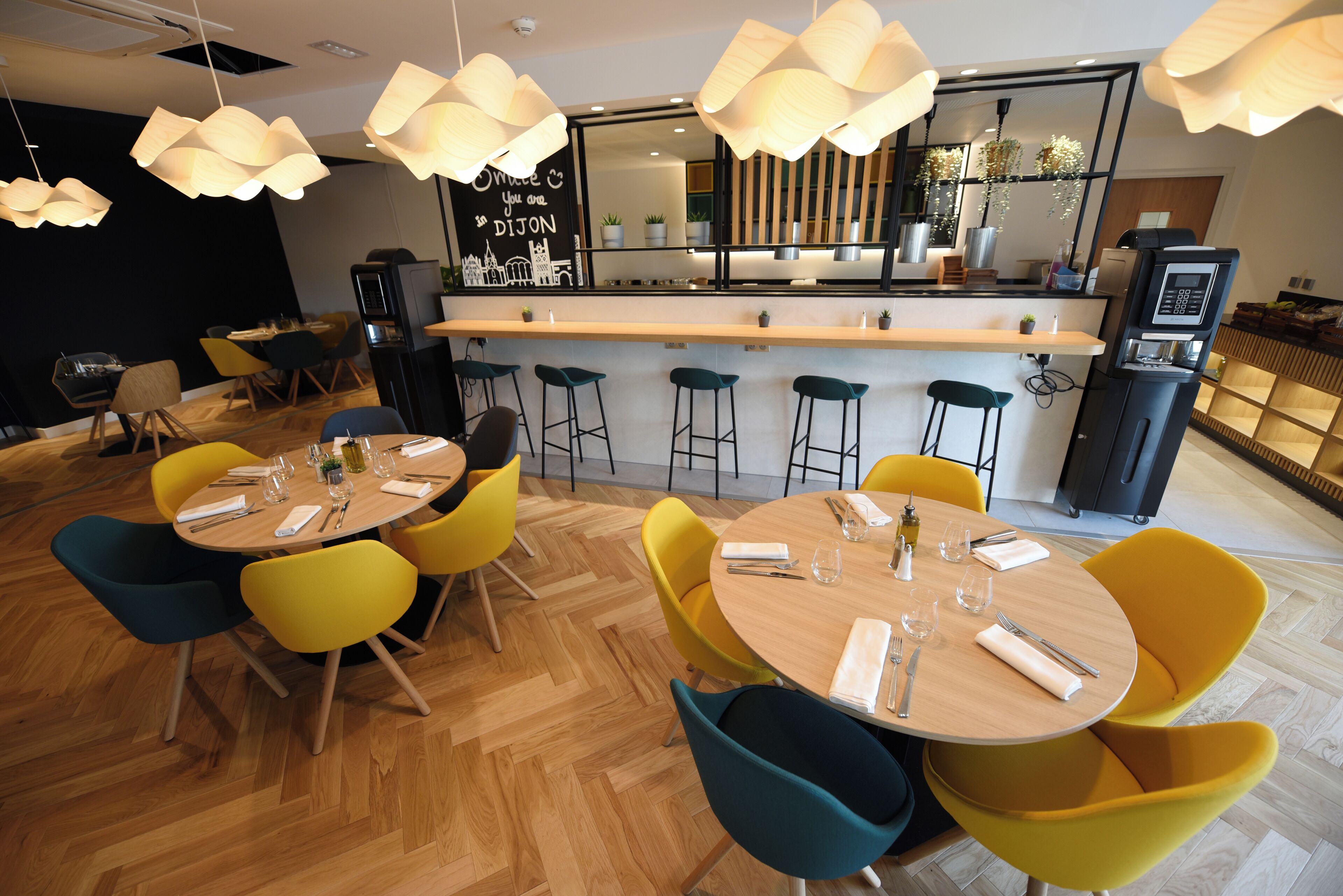 Un restaurante moderno con mesas redondas y sillas amarillas llamativas, una zona de bar con taburetes y un menú a la vista.