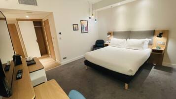 Une chambre d’hôtel avec un grand lit, des tables de chevet, un bureau avec une chaise et une armoire.