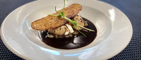 Un plato con un guiso, posiblemente de pescado, acompañado de rebanadas de pan y una salsa oscura.