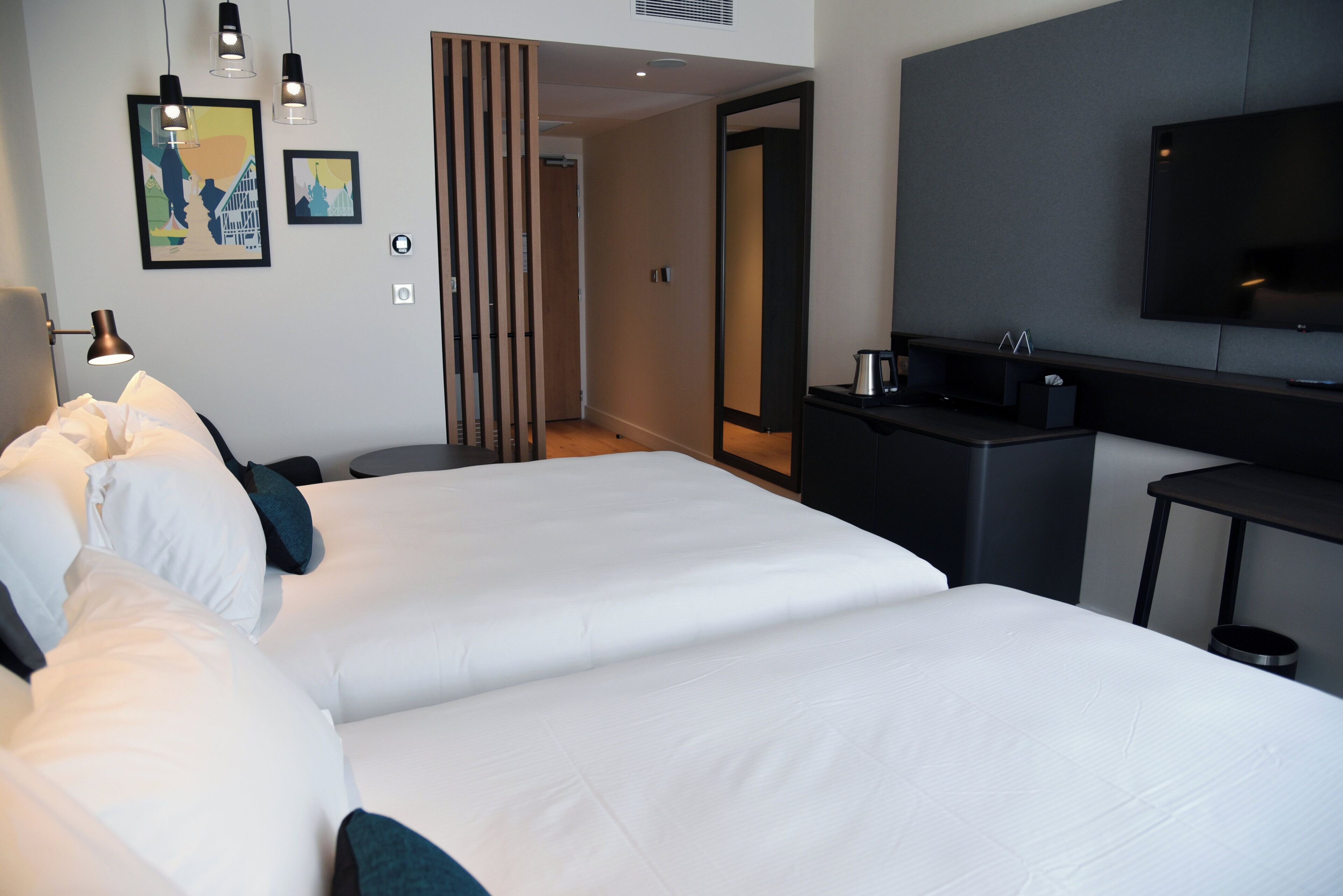 Une chambre d’hôtel avec deux lits, un bureau, une télévision et des œuvres d’art accrochées au mur.