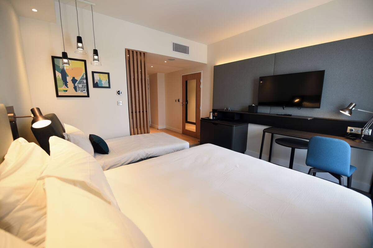 A hotel room with two beds, a desk, a TV, and a chair.