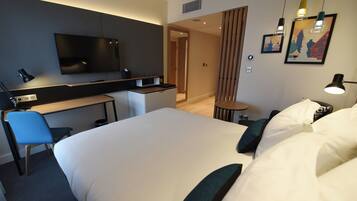 A hotel room with a large bed, a desk with a chair, a television, and a small table.