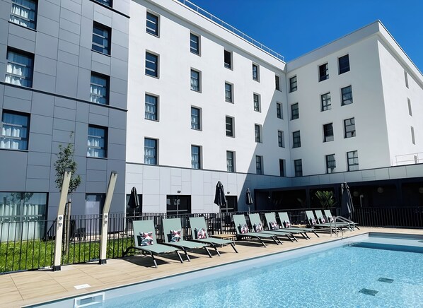 Un hotel moderno con piscina, sillones de descanso y un jardín bien cuidado.