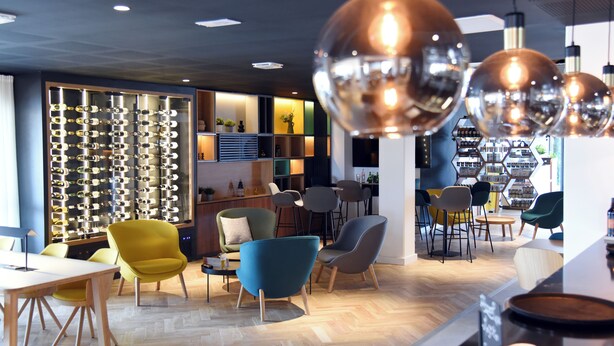 A modern interior with a variety of seating options, a display of eyeglasses, and pendant lighting. - Holiday Inn Dijon Sud Longvic by IHG (Longvic)