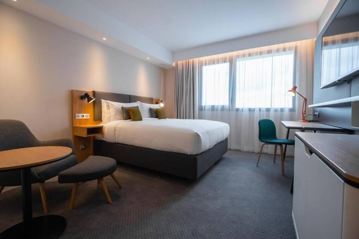 A hotel room with a bed, desk, chair, and a TV.