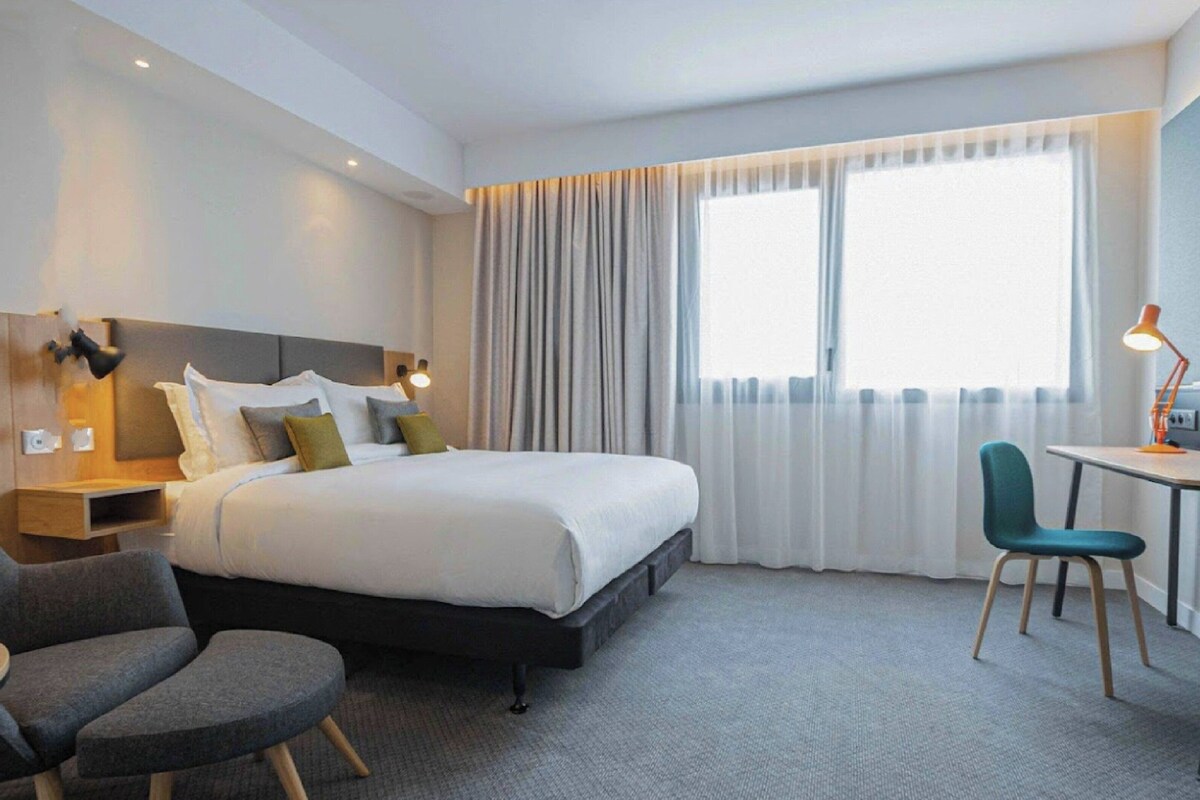 A hotel room with a bed, a desk, a chair, and a small table.