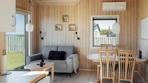 Une pièce confortable avec un canapé, une petite table et un coin repas avec des chaises. Des lampes sont fixées au mur et une fenêtre offre une vue sur l’extérieur.