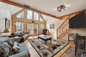 A spacious living room with a large window, a sofa, a coffee table, and a staircase.