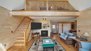 Um quarto estilo loft com escada de madeira, lareira, televisão e sofá.