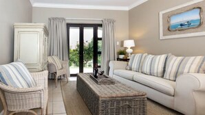 Un salon comprenant un canapé, deux fauteuils, une table basse et une vue sur l’extérieur, accessible par une porte vitrée.