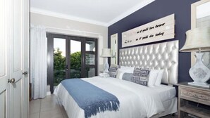 Une chambre avec un grand lit, une tête de lit ornée d’une citation, une table de chevet et une vue sur l’extérieur, visible à travers une porte vitrée.