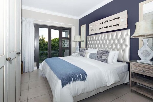 A bedroom with a large bed, a headboard with a quote, a nightstand, and a view through a glass door.