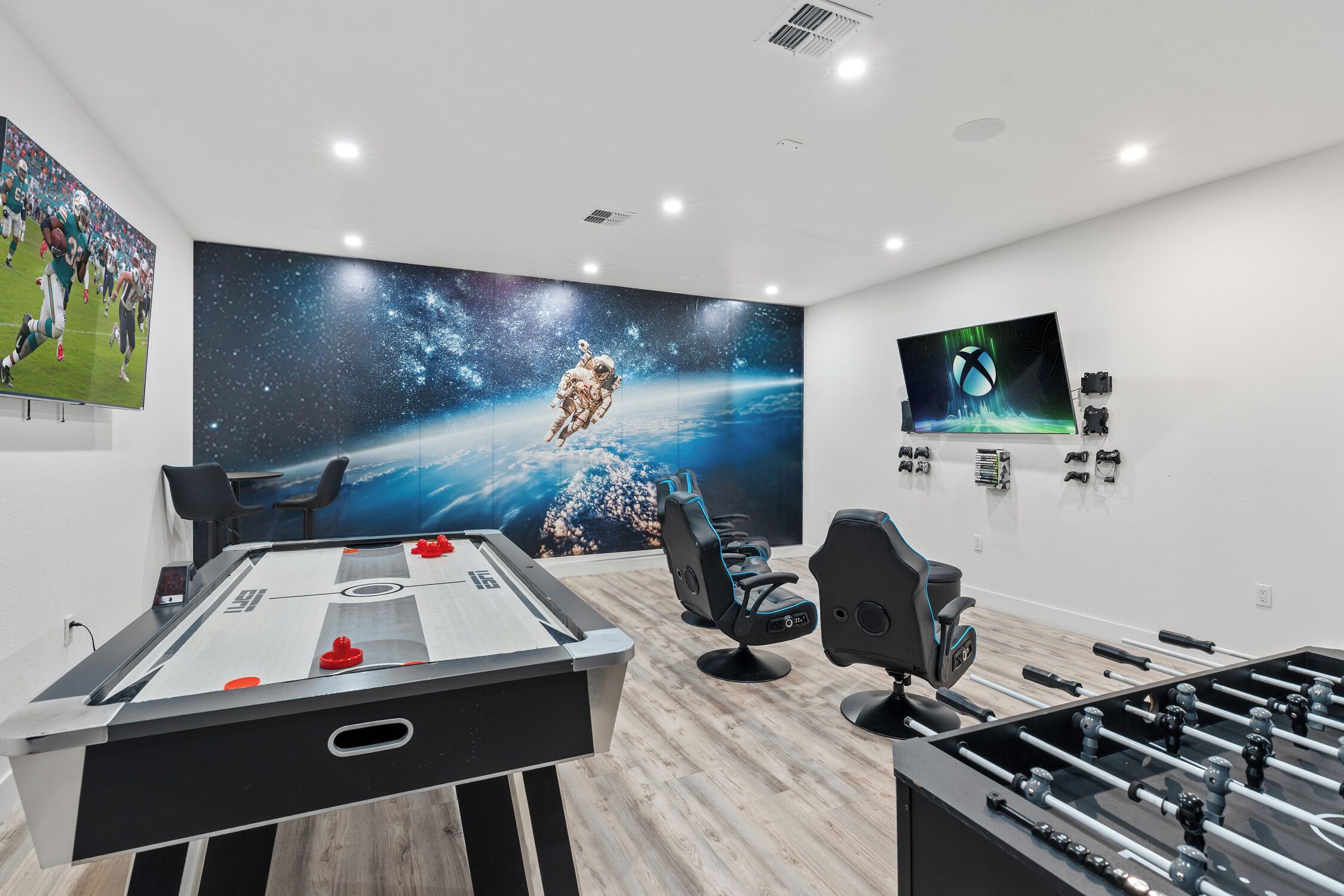A room with a foosball table, a pool table, and a large screen displaying a space-themed image.