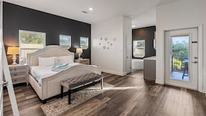 Ein Schlafzimmer mit einem großen Bett, Nachttischen, einer Bank und Blick ins Freie durch eine Schiebetür.
