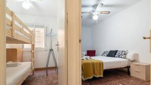 A room with a bunk bed, a desk, a chair, a wardrobe, and a bed with a patterned blanket. - Apartament Sant Mateu (Vilassar de Mar)