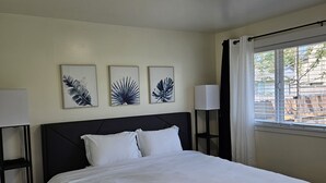 Ein Schlafzimmer mit einem Bett, zwei Nachttischlampen und drei Wandbildern mit Blattformen.