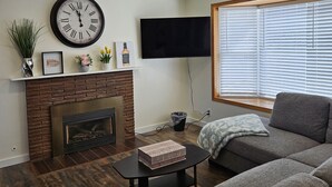 Ein Wohnzimmer mit Kamin, einer großen Uhr, einem Flachbildfernseher und einem Sofa.