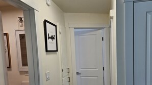 Ein Flur mit Holzboden, weißen Wänden und einer Deckenleuchte. Rechts eine Tür und links eine Tür mit einem Bilderrahmen.