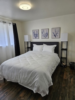 A neatly made bed with white linens, a dark wooden floor, and three framed wall art pieces above it.