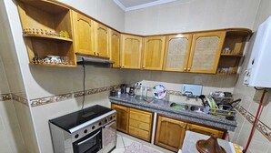 A compact kitchen with wooden cabinets, a stove, and a sink. - Appartement (Tangier)
